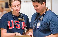 Female with USA shirt on and male in scrubs looking at chart.