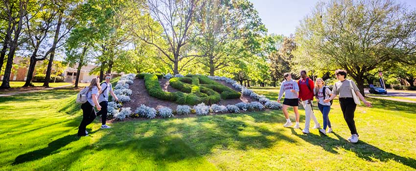 Students walking by USA sign on grass.